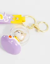Llavero con dije de gatito dentro de una burbuja con base lila y correa de silicona lila con diseño de letras y dibujos en amarillo y blanco.