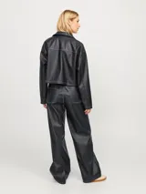 Campera corta de cuero sintético negra con cuello clásico, cierre frontal con cremallera, bolsillos con solapa en el pecho y costuras blancas en contraste.