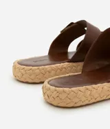 Sandalias marrones con dos tiras anchas con hebillas plateadas y suela plana con textura de rafia.