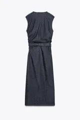 Vestido midi de denim azul oscuro, con cuello redondo y sin mangas. Presenta detalle de frunces en la cintura, cinturón elástico con hebilla dorada y cierre lateral con cremallera oculta. Tiene falsos botones delanteros.