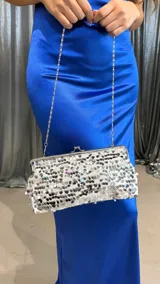 Cartera de mano plateada cubierta de lentejuelas, con cierre metálico y cadena plateada fina para colgar al hombro.