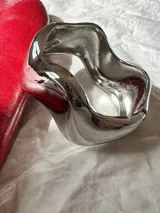 Brazalete rígido plateado con diseño irregular y anillo a juego.