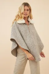 Poncho de lana color beige con cuello de piel sintética blanca desmontable y cierre frontal con cremallera dorada. Diseño amplio y cómodo.