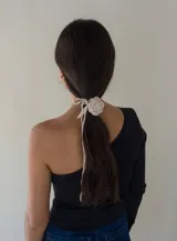 Gargantilla tejida a mano en forma de rosa color crudo, hecha con hilados de algodón sobrantes de tejidos. Tiene una tira removible para usarla como collar o cinturón.