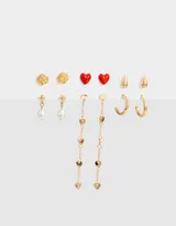 Set de seis pares de aros dorados con distintos diseños: aros tipo botón con forma de flor, aros con forma de corazón rojo, aros con forma de gota, aros tipo argolla y aros colgantes con perlas y corazones.