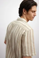 Camisa de manga corta con cuello resort y cierre frontal con botones. Diseño a rayas verticales en tonos beige y blanco.