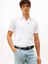 Camisa de manga corta blanca con textura seersucker, cuello clásico y cierre frontal de botones. Presenta un pequeño logo bordado en el pecho.