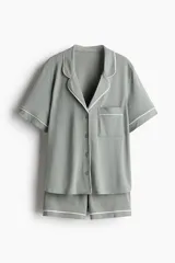 Pijama corto de dos piezas color gris con ribetes blancos. Camisa de manga corta con cuello abierto, botones adelante, hombros caídos y bolsillo superior. Short con elástico en la cintura.