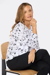 Blusa blanca de manga larga con estampado floral en negro, cuello redondo y botones personalizados.