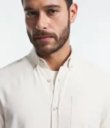 Camisa de hombre de corte regular, color borgoña, confeccionada en tela Oxford con efecto jaspeado. Tiene cuello inglés, abotonadura frontal, mangas largas con puños abotonados y bolsillo de parche en el pecho.