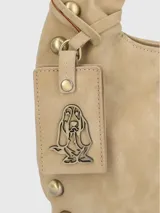 Cartera tipo hobo color beige de gamuza sintética con tachas doradas en el borde. Tiene un asa de hombro y un dije colgante con el logo de la marca.
