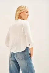 Camisa blanca de manga larga con cuello redondo y bordado floral en el delantero. El delantero es de algodón plano, mientras que las mangas y la espalda son de jersey a tono. Presenta un efecto fruncido en el centro de la espalda y puños en las mangas largas.