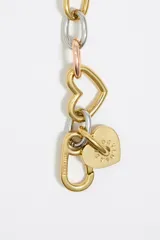 Pulsera de cadena metálica con eslabones en dorado, plateado y cobre. Incluye dijes de corazones y un dije redondo con el logo de la marca grabado.