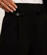 Pantalón de vestir negro de corte wide leg, confeccionado en crepé. Presenta cintura con trabillas, detalle de solapa con botón y bolsillos laterales.