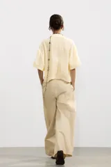 Camisa color amarillo pálido de tejido fluido, con cuello solapa, escote pico, manga corta, bolsillo de parche en el pecho y cierre frontal con botones.