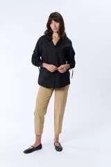 Camisa negra de manga larga con cuello clásico y cierre frontal con botones. Las mangas tienen frunces y lazos para ajustar el largo.