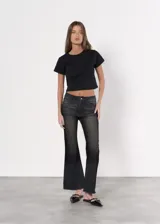 Pantalón de jean negro con efecto lavado, corte ajustado en la cadera y acampanado desde la rodilla, con terminación desflecada.
