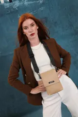 Bandolera tipo phone bag pequeña, color marrón claro, con correa de galón regulable. Tiene un compartimento principal y un bolsillo adicional con tapa.