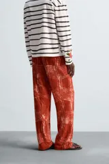 Pantalón relaxed fit de punto ligero tejido en hilatura de algodón color ladrillo con estampado a cuadros difuminados en blanco. Cintura elástica ajustable con cordón y bolsillos laterales.