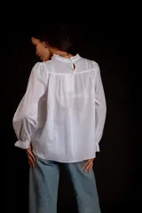 Camisa color crema con cuello alto y mangas largas con volados en los puños. Presenta detalles de crochet y broderie en el frente.