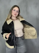 Campera negra de cuero sintético con interior y cuello de corderito color beige, cierre frontal con cremallera y hebillas ajustables en el cuello y la cintura.