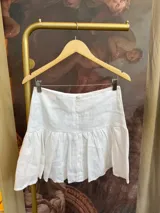 Minifalda blanca acampanada de lino, tiro medio/alto y cierre invisible en la espalda.