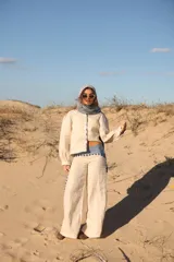 Pantalón de lino color crudo, de corte ancho y tiro medio. Presenta detalles de rayas verticales en color marrón y celeste en los laterales y en la cintura.