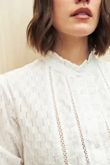 Camisa blanca de manga 3/4 confeccionada en algodón liviano con diseño calado y detalles de encaje en el frente. Cuello con volados.