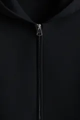 Campera con capucha negra, de tejido efecto neopreno, con cierre frontal y bolsillos abiertos. Presenta un corte holgado y hombros caídos.
