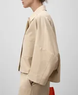 Camisa color beige de corte cuadrado y amplio, con cuello solapa, mangas 3/4 y bolsillo de parche en el pecho. Cierre frontal con botonadura oculta.
