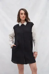 Camisa larga de lino color beige, con cuello camisero y cierre frontal con botones. Tiene mangas largas con puños abotonados, bolsillos laterales y una franja a contratono en la espalda y mangas.