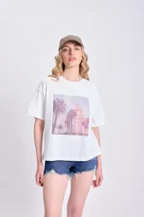 Remera blanca de corte cuadrado con estampa fotográfica de palmeras y edificio.