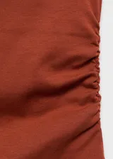 Camiseta sin mangas, ajustada al cuerpo, color terracota/óxido, con cuello perkins y fruncidos laterales.