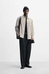 Camisa color crema de corte relaxed fit, confeccionada en tejido de mezcla de algodón suave al tacto. Tiene cuello solapa, manga larga con puños abotonados, un bolsillo de parche en el pecho y cierre frontal con botones.