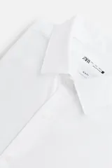 Camisa blanca de corte regular fit, con cuello italiano, manga larga con puños abotonados y cierre frontal con botones.