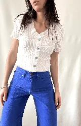 Camisa blanca con textura y botones decorativos en el frente, de manga corta y corte ajustado.