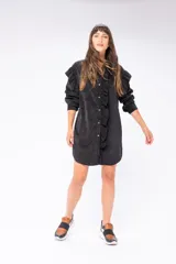 Camisa larga negra de poliéster con textura de pana fina, con mangas largas y cierre frontal con botones. Presenta volados verticales en el frente.