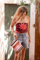 Sobre de algodón a rayas verticales de colores naranja, rosa, marrón, rojo y blanco. Tiene cierre superior con cremallera y tira de cuero marrón para la muñeca.