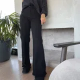 Pantalón jean negro de corte acampanado con aberturas laterales y ruedo desflecado.