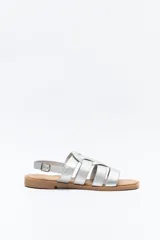 Sandalias plateadas de cuero sintético con tiras anchas cruzadas y detalle central calado. Cierre con hebilla ajustable y suela plana color suela.