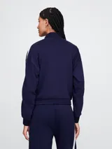 Campera deportiva Gap azul marino con cierre frontal, cuello alto y logo bordado en el pecho. Presenta dos líneas blancas verticales a lo largo de las mangas.