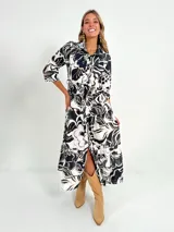 Vestido largo camisero con estampado floral en tonos rosados y blancos, con cuello camisero, manga 3/4 y falda escalonada. Incluye cinturón fino de soga.