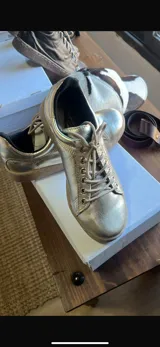 Zapatillas acordonadas de cuero color marrón con detalles dorados en el talón y suela blanca.