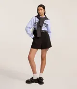 Short de sastrería negro, corte recto, con cintura alta, trabillas, pliegues frontales y detalle de medio cinturón con hebilla lateral.