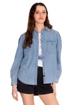 Camisa de manga larga celeste de denim con dos bolsillos en el pecho y cierre con botones metálicos.