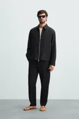 Pantalón negro de corte regular fit, confeccionado en tejido de lino. Presenta cintura con botón y cierre de cremallera, bolsillos frontales y bolsillos traseros de doble vivo.
