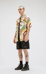 Camisa de manga corta con calce oversize y estampado abstracto en tonos naranja, verde, amarillo y marrón.