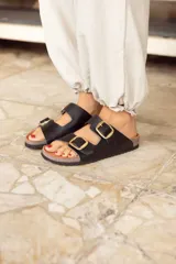 Sandalias negras con dos tiras anchas ajustables con hebillas doradas. Plataforma de corcho y suela de goma.