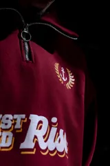 Buzo de algodón color bordó, estilo universitario, con cierre medio frontal y cuello alto. Estampado frontal con el texto "Since 19" y un ancla con laureles en amarillo y blanco.