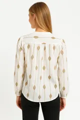 Blusa color crema con estampado de hojas color marrón, cuello mao con abertura y botones, mangas largas abullonadas con puños elásticos.